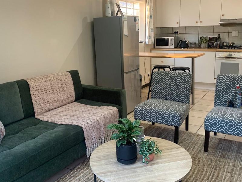 Open-plan living area featuring a functional kitchen with built-in cabinetry, gas hob, and oven, seamlessly connected to a comfortable lounge space with tiled flooring.