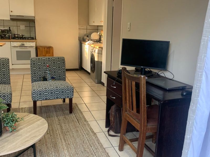 Open-plan living area featuring a functional kitchen with built-in oven, hob, and tiled flooring, seamlessly connected to a versatile workspace.