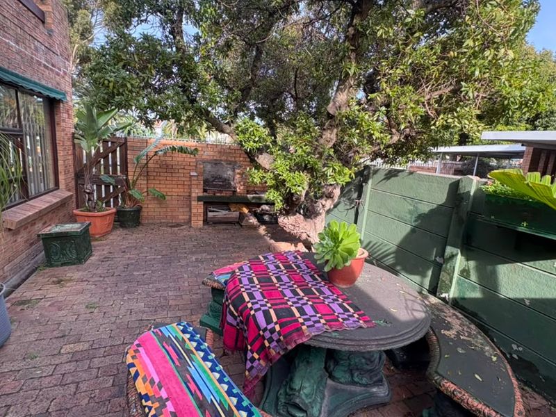 A private rear courtyard featuring brick paving, a built-in braai area, and established trees, providing a functional outdoor entertainment space.
