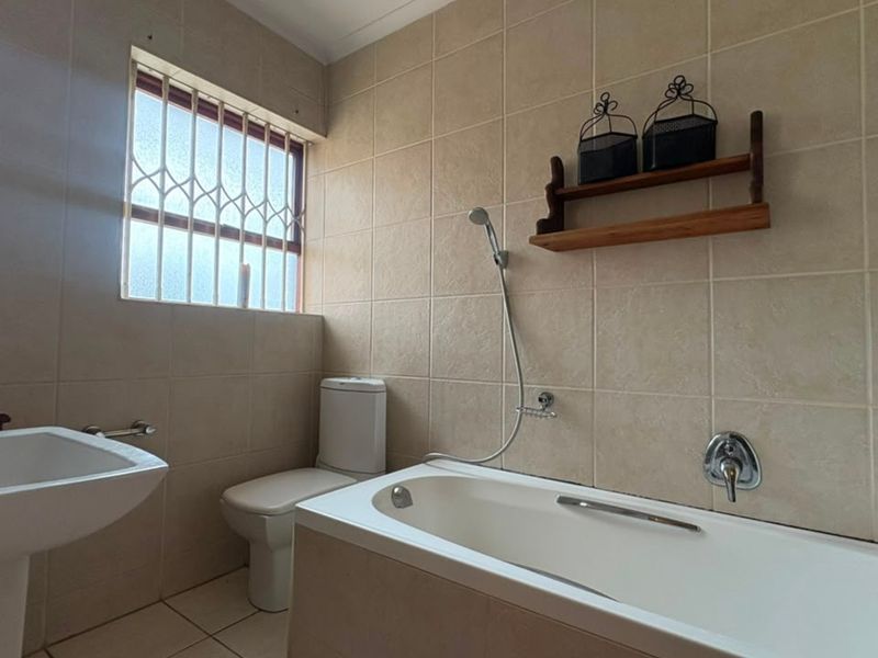 A functional bathroom featuring a bathtub with a handheld shower, a pedestal basin, and a toilet, finished with neutral wall and floor tiles.