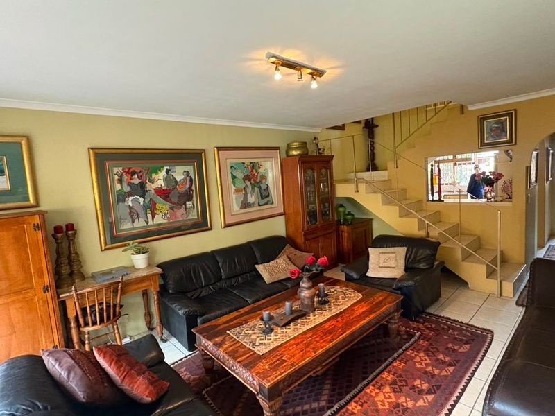 Spacious living room featuring tiled flooring, a central staircase, and an archway leading to the rear of the property.
