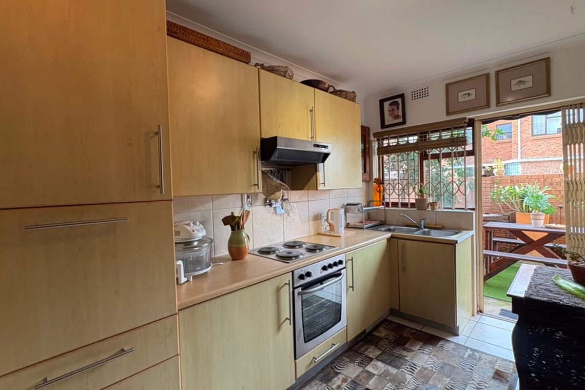 Functional kitchen featuring light wood-finish cabinetry, integrated electric hob and oven, tiled backsplash, and direct access to an outdoor patio area.