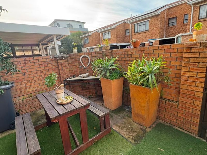 A private rear courtyard featuring a brick boundary wall, artificial turf, and paved sections, providing a compact outdoor space for relaxation.
