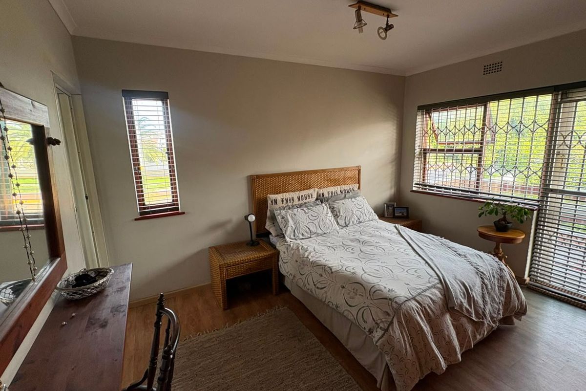 A well-lit bedroom featuring laminate flooring, security bars on windows, and neutral wall finishes, providing a functional and comfortable sleeping space.