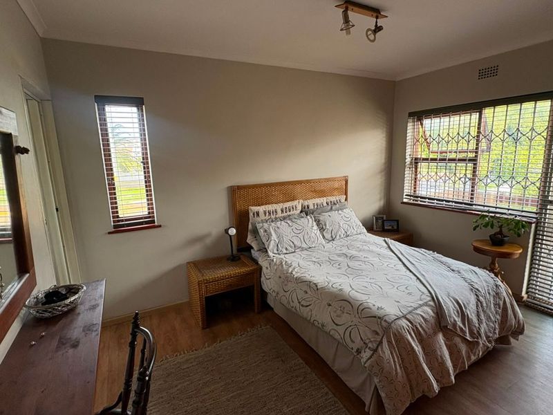 A well-lit bedroom featuring laminate flooring, security bars on windows, and neutral wall finishes, providing a functional and comfortable sleeping space.