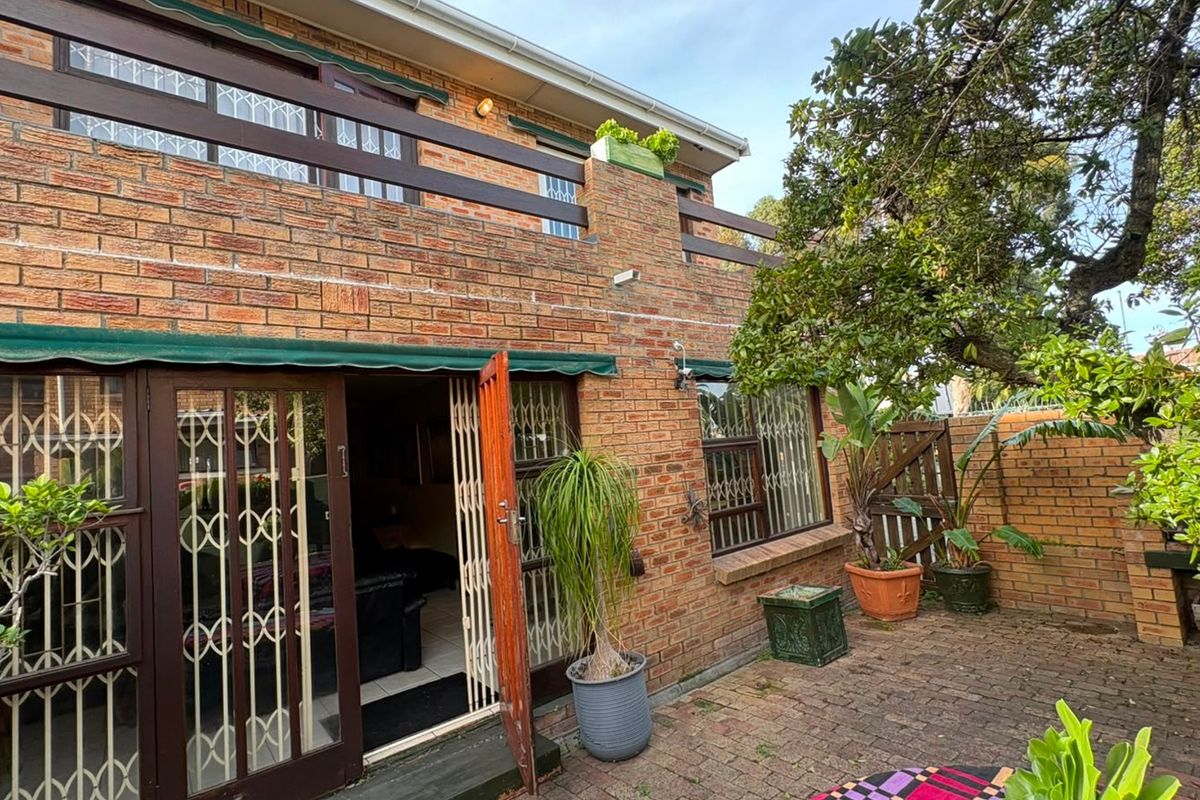 Rear exterior view of a brick townhouse featuring a paved patio area, upper-level balcony with timber railing, and secure access points.