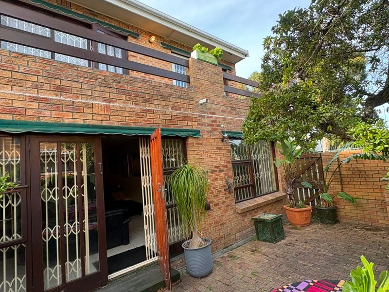 Rear exterior view of a brick townhouse featuring a paved patio area, upper-level balcony with timber railing, and secure access points.