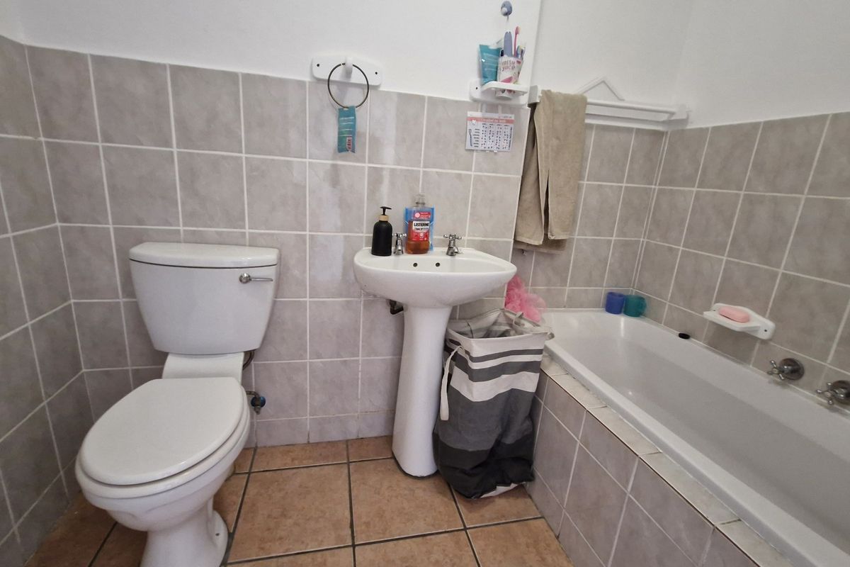 A functional bathroom featuring a pedestal basin, toilet, and bathtub with neutral wall and floor tiling.