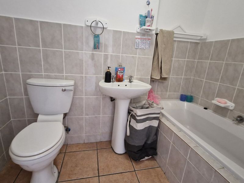 A functional bathroom featuring a pedestal basin, toilet, and bathtub with neutral wall and floor tiling.