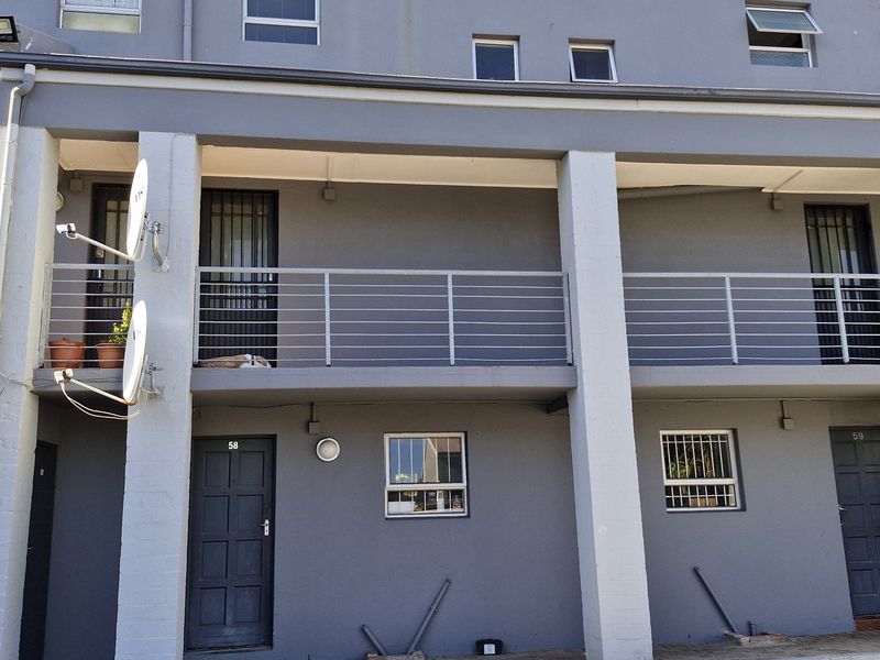 Exterior view of an apartment building featuring a shared balcony with metal railings, security gates, and ground-level access points.