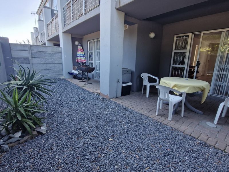 A ground floor patio area featuring paved flooring, a gravel garden section, and secure sliding door access to the apartment interior.