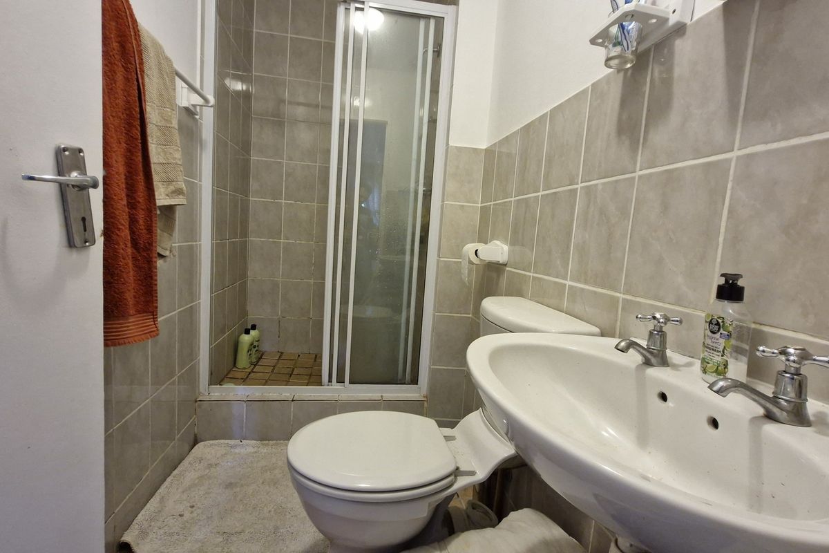 A functional bathroom featuring a shower enclosure, pedestal washbasin, and toilet with neutral wall tiling.