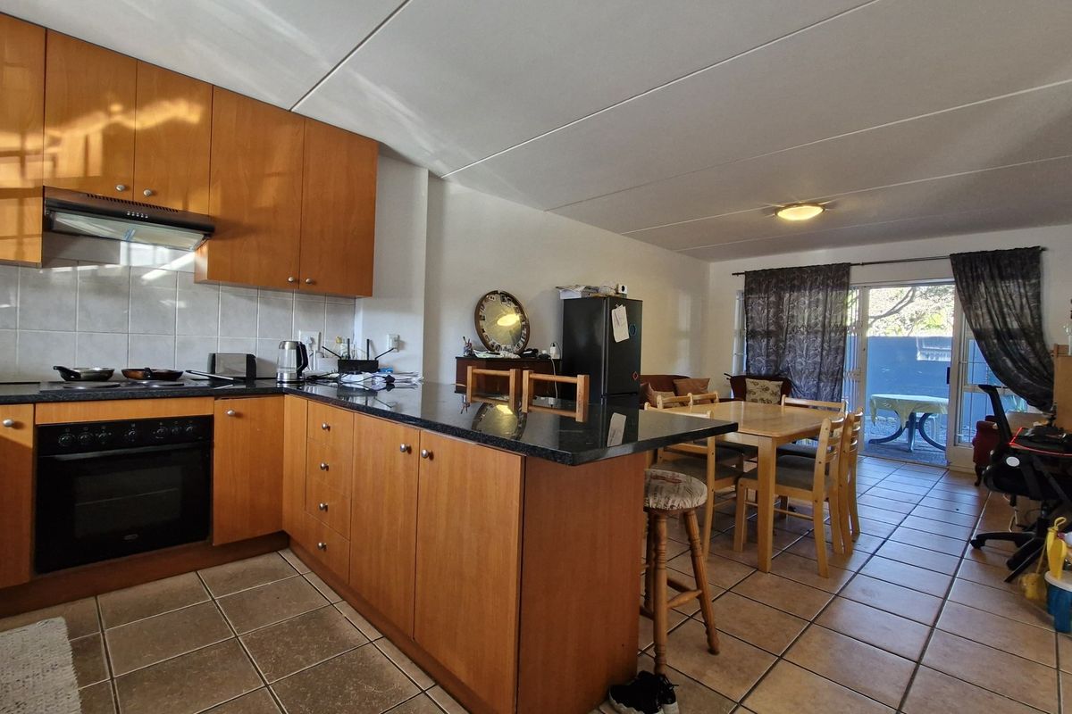 Open-plan kitchen and living area featuring wooden cabinetry, granite countertops, built-in oven, and tiled flooring with direct access to an outdoor patio.