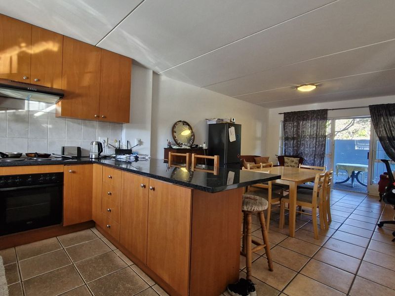 Open-plan kitchen and living area featuring wooden cabinetry, granite countertops, built-in oven, and tiled flooring with direct access to an outdoor patio.