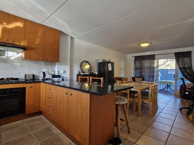Open-plan kitchen and dining area featuring wood-finish cabinetry, granite countertops, tiled flooring, and direct access to an outdoor patio through sliding glass doors.