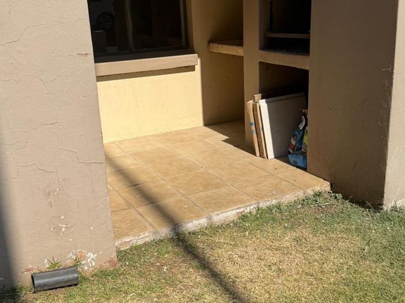 Outdoor patio area featuring a built-in braai, tiled flooring, and an exterior water tap, requiring some maintenance to the wall plaster and paintwork.