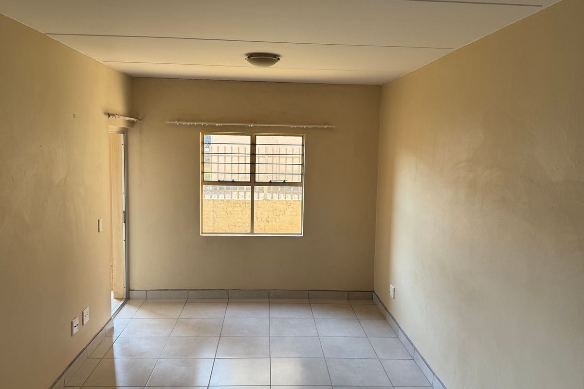 An empty living room featuring tiled flooring, a window with security bars, and a sliding door leading to an outdoor area.