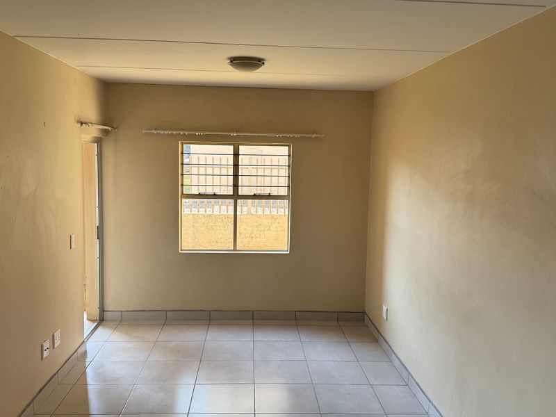 An empty living room featuring tiled flooring, a window with security bars, and a sliding door leading to an outdoor area.