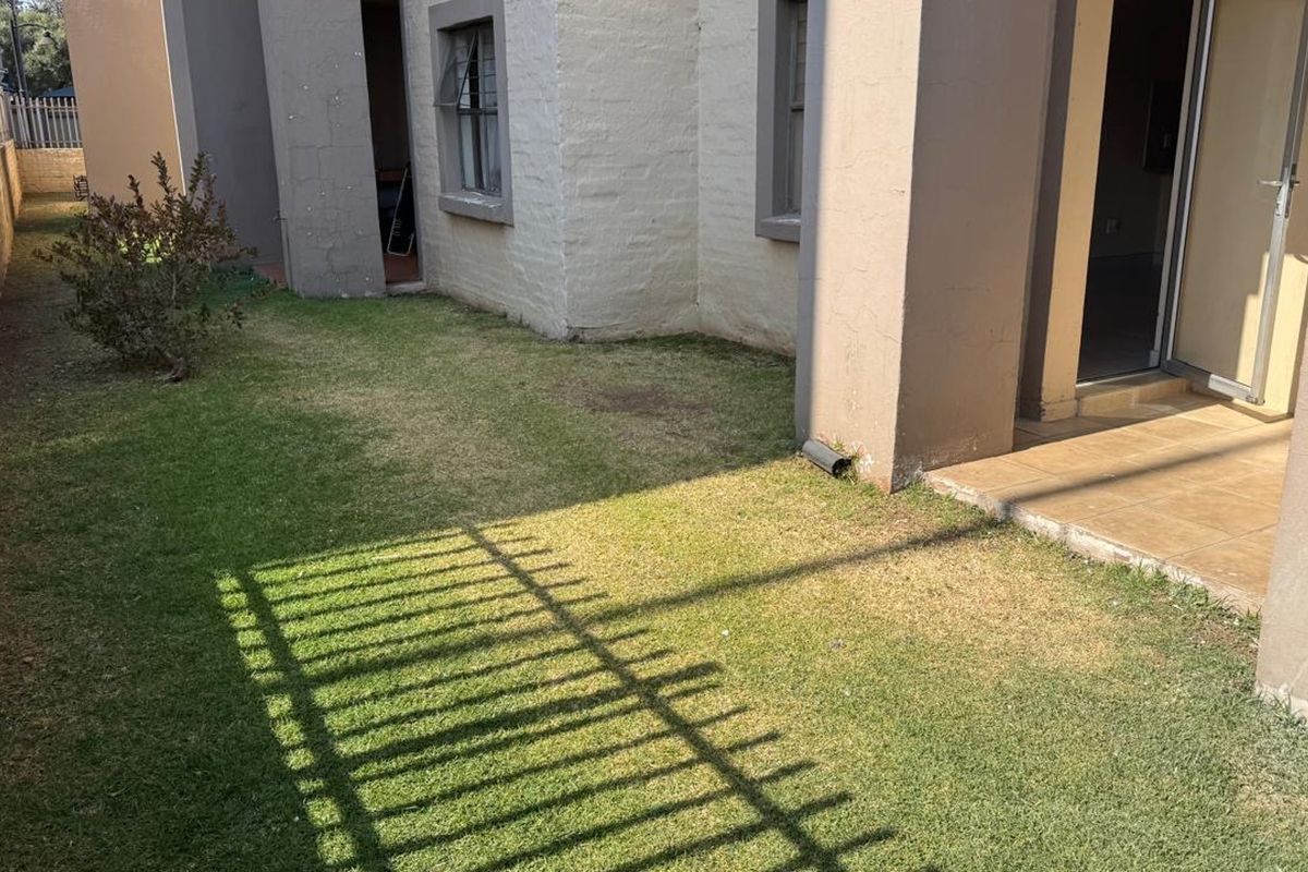 A rear exterior view of the apartment featuring a small private lawn, a tiled patio area, and perimeter fencing.