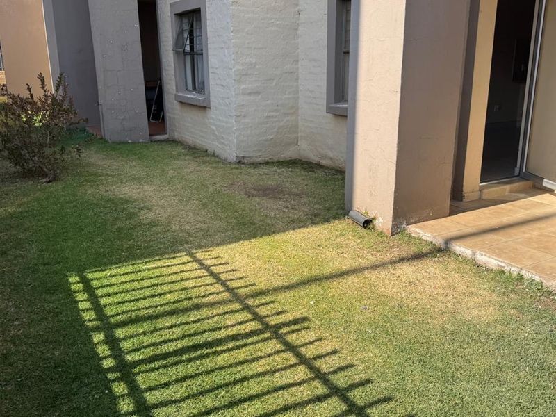 A rear exterior view of the apartment featuring a small private lawn, a tiled patio area, and perimeter fencing.