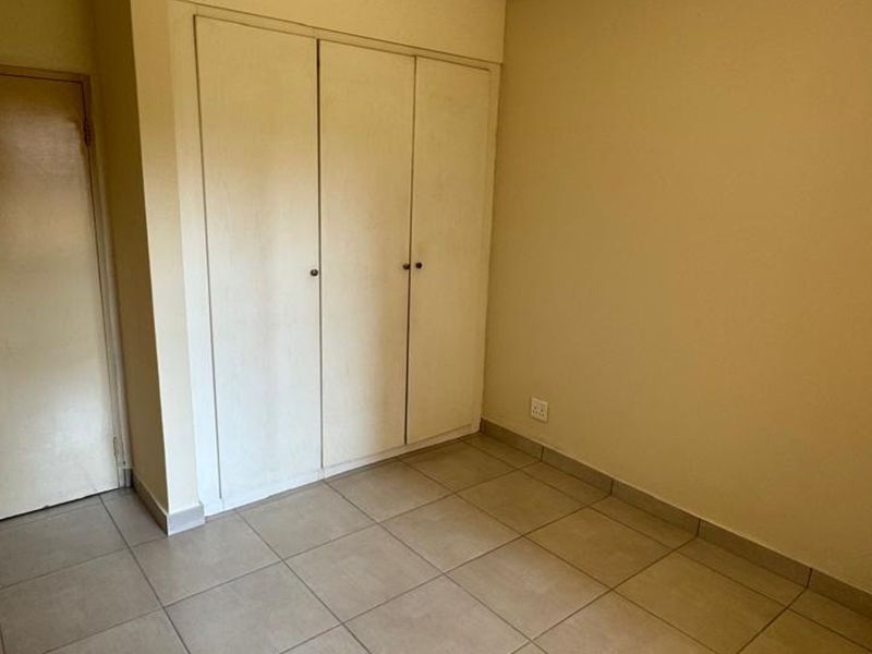 A clean, empty bedroom featuring neutral tiled flooring and built-in storage cupboards, providing a versatile space ready for personalization.