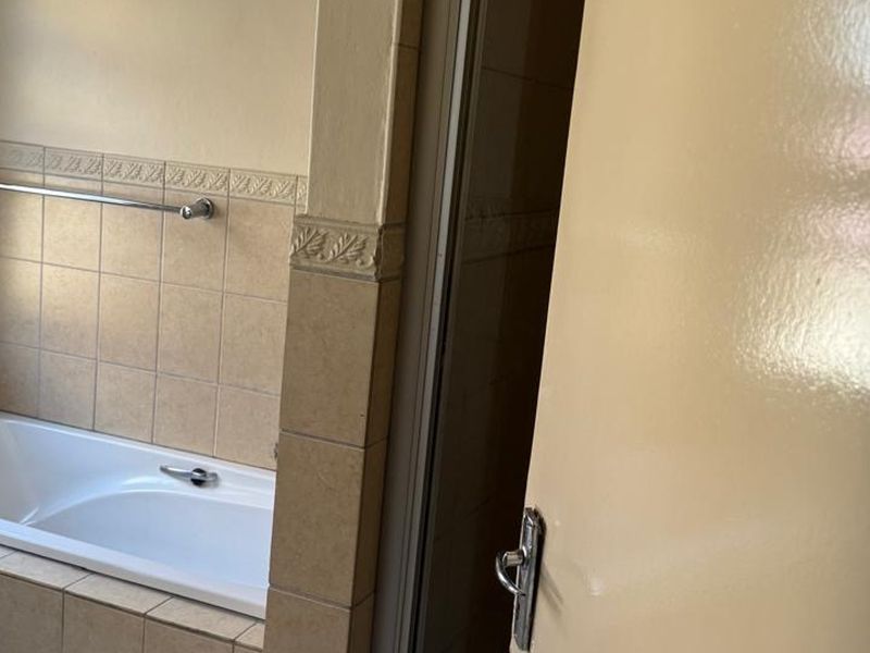 A functional bathroom featuring a built-in bathtub with neutral wall tiling and a chrome towel rail.