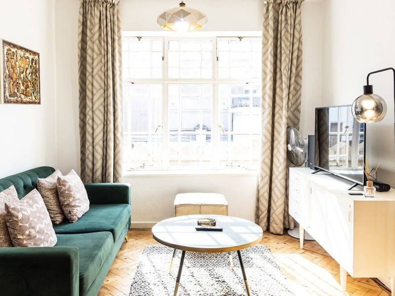 A bright living room featuring classic parquet flooring, a large multi-pane window, and neutral wall finishes, creating a warm and inviting atmosphere.