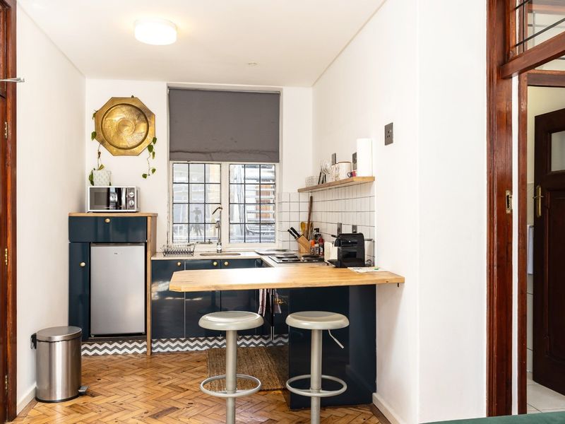 Compact kitchen featuring dark blue cabinetry, wooden countertops, a breakfast bar, and classic parquet flooring, complemented by traditional timber door frames.