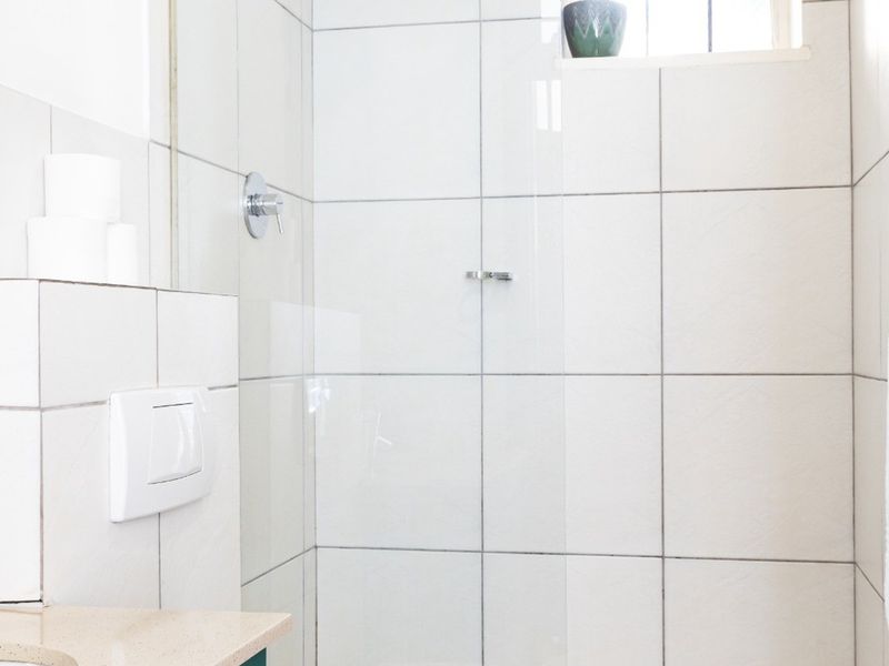 A functional bathroom featuring a glass-enclosed shower, tiled walls, and a vanity basin with modern fixtures.