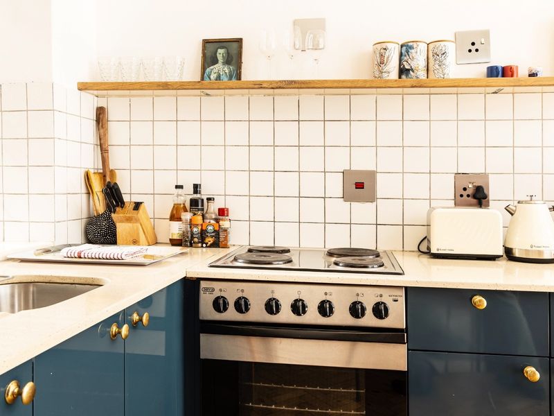 A well-maintained kitchen featuring blue cabinetry, stone countertops, a tiled backsplash, and a built-in electric oven with a hob.