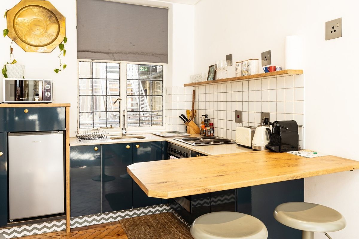 Compact kitchen featuring dark blue cabinetry, a wooden breakfast bar, tiled backsplash, and integrated cooking appliances with herringbone flooring.