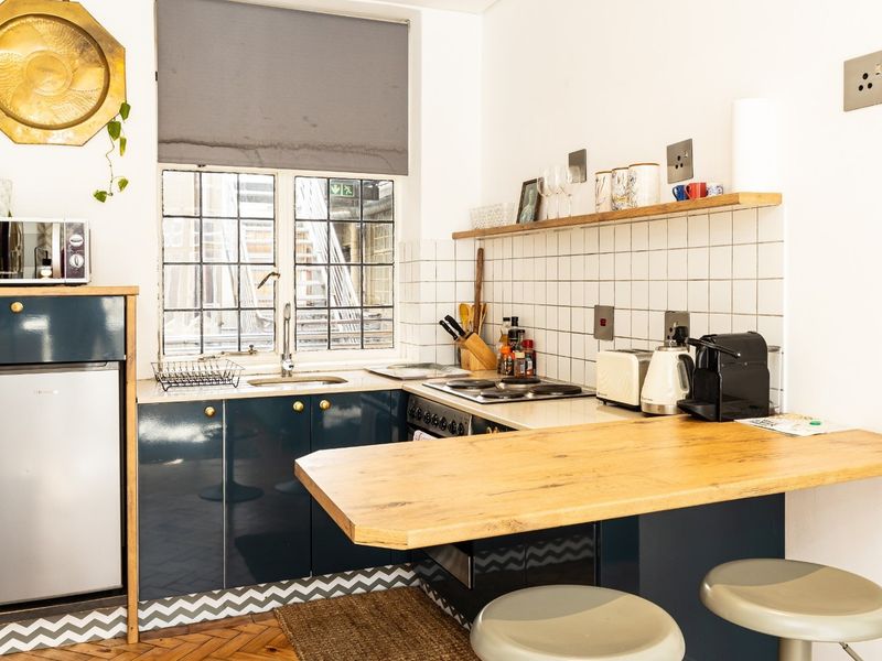 Compact kitchen featuring dark blue cabinetry, a wooden breakfast bar, tiled backsplash, and integrated cooking appliances with herringbone flooring.