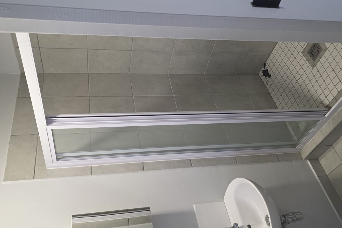 A compact bathroom featuring a wall-mounted basin, mirrored medicine cabinet, and a tiled shower enclosure with a glass door.