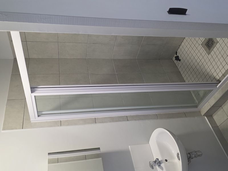A compact bathroom featuring a wall-mounted basin, mirrored medicine cabinet, and a tiled shower enclosure with a glass door.