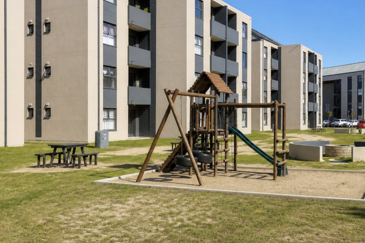 Communal outdoor area featuring a playground, sand pit, and concrete fire pit situated between modern apartment blocks.