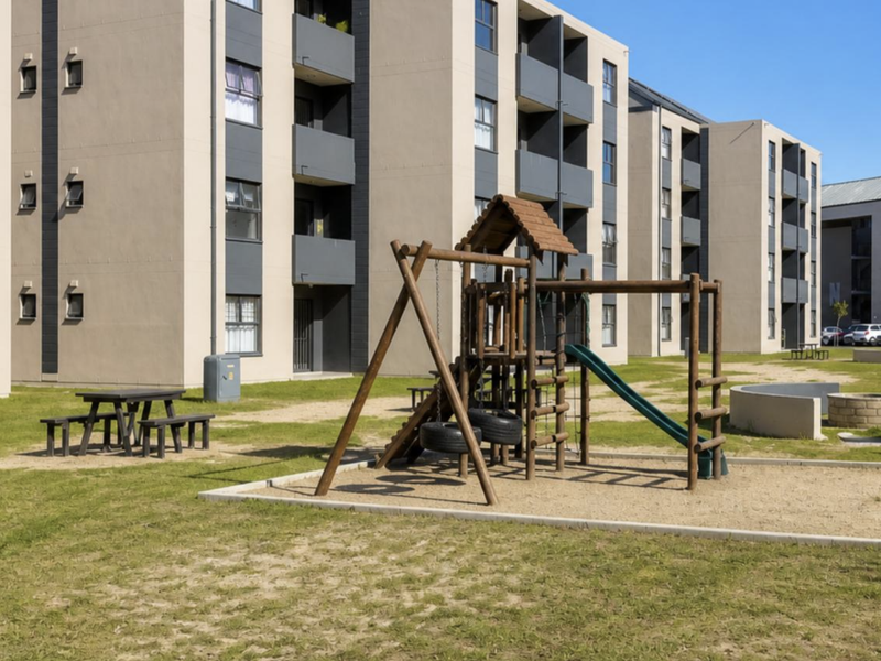 Communal outdoor area featuring a playground, sand pit, and concrete fire pit situated between modern apartment blocks.