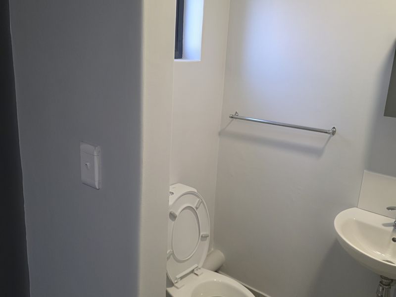 A compact, clean bathroom featuring a wall-mounted basin, a standard toilet, and a towel rail, finished with neutral wall paint.