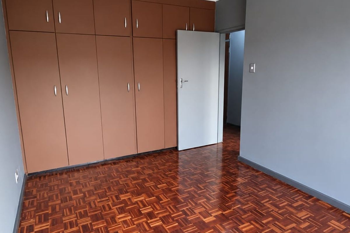 A clean, empty bedroom featuring polished parquet flooring and extensive built-in wooden cupboards, offering a neutral canvas for personalization.