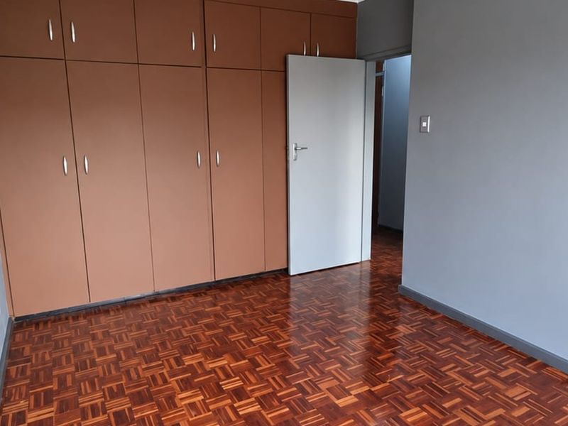 A clean, empty bedroom featuring polished parquet flooring and extensive built-in wooden cupboards, offering a neutral canvas for personalization.