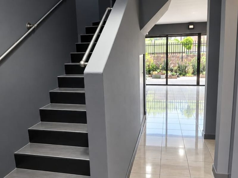 Modern entrance hall featuring a sleek staircase with metal handrail, polished tiled flooring, and large sliding glass doors leading to the rear garden.