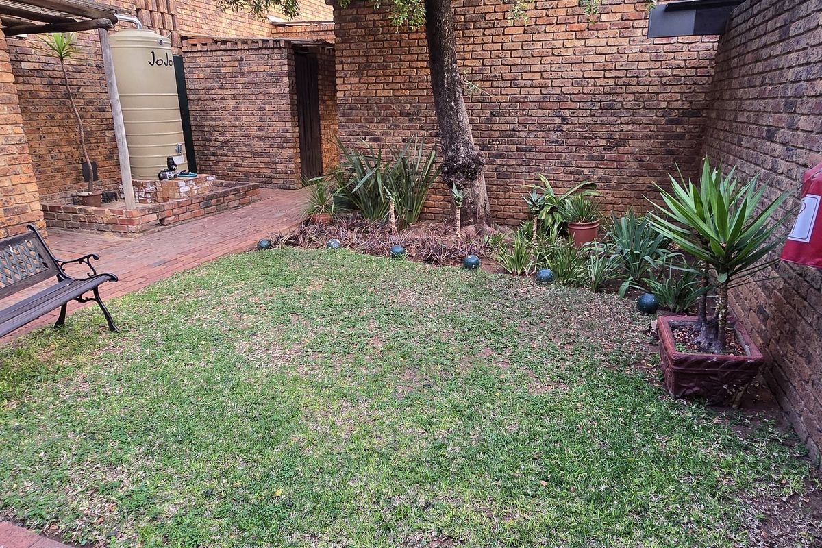 A private rear courtyard featuring a brick-walled garden, paved pathway, and a water storage tank, offering a functional outdoor space for the townhouse.