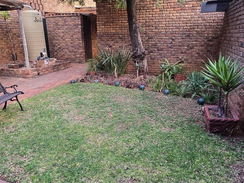 A private rear courtyard featuring a brick-walled garden, paved pathway, and a water storage tank, offering a functional outdoor space for the townhouse.