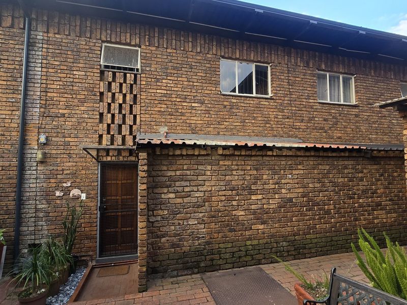 Rear exterior view of a face brick townhouse featuring a paved courtyard area, security gate, and multiple windows.