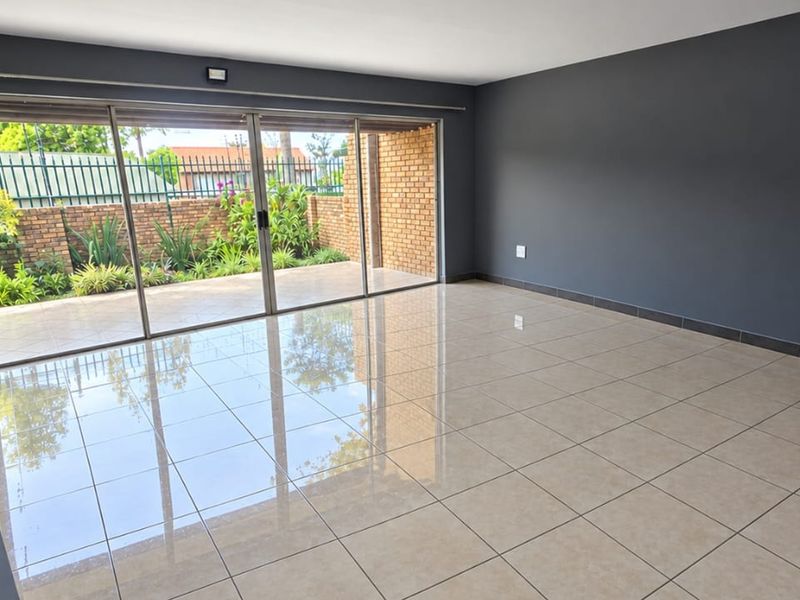 Spacious, empty living area featuring large sliding glass doors that open onto a private patio, finished with neutral floor tiles and dark accent walls.