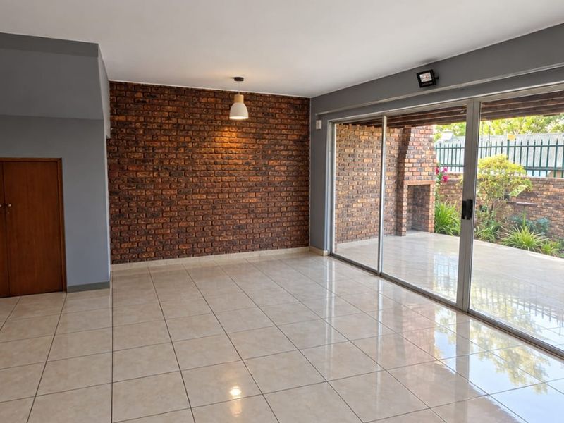 Spacious living area featuring an exposed brick accent wall, large sliding glass doors leading to a patio, and neutral tiled flooring.