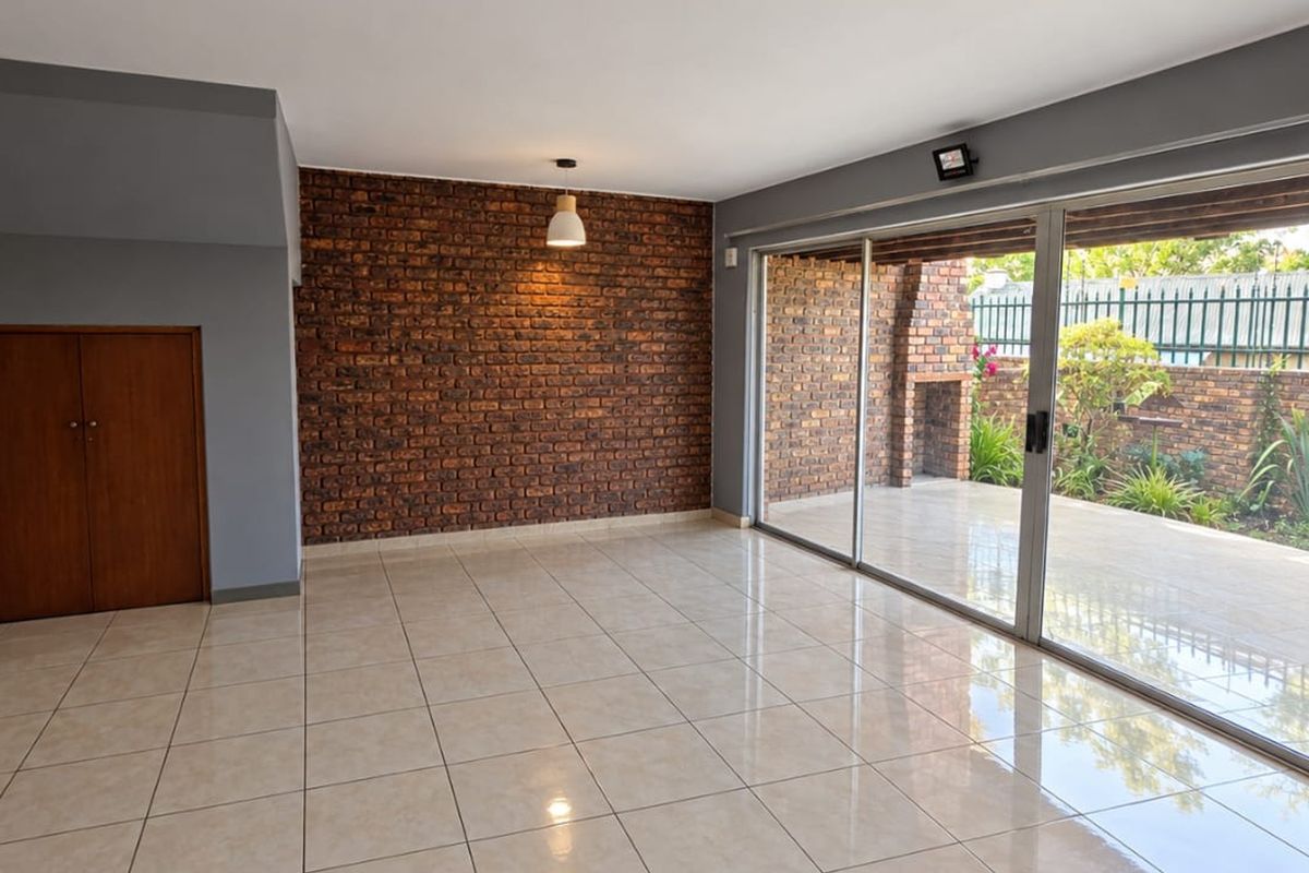 Spacious living area featuring an exposed brick accent wall, large sliding glass doors leading to a patio, and neutral tiled flooring.