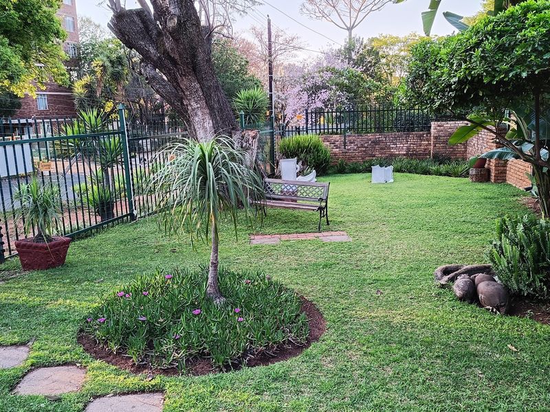 A well-maintained private garden featuring established trees, landscaped garden beds, paved stepping stones, and secure perimeter fencing.