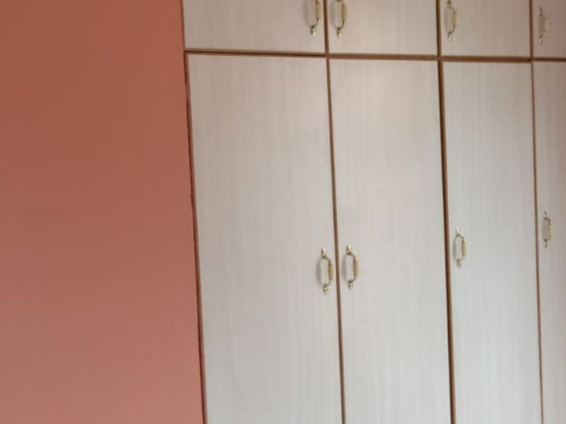 A bedroom interior featuring light-toned built-in cupboards with classic hardware against peach-colored walls.