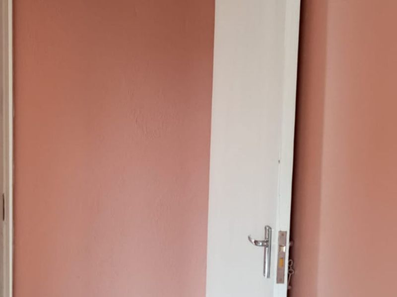 A close-up view of a plain interior wall painted in a muted pink tone with a white door frame and handle.