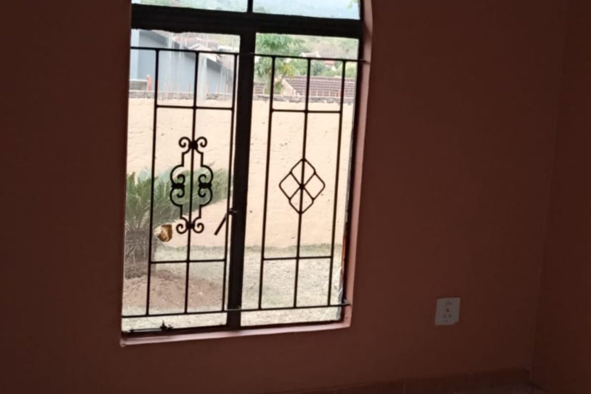 An empty bedroom featuring security bars on the window and basic electrical fixtures, requiring cosmetic updates to the wall finishes.